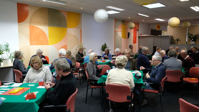 Zaal met spelers en een boekenkast langs de wand