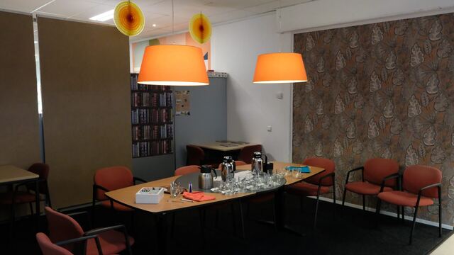 Vergadertafel met oranje hanglampen en boekenkast