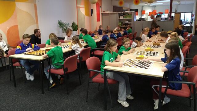 Kinderen in clubshirts spelen dammen aan lange tafels